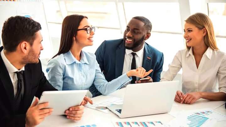Four business professionals sit at a table with documents and a tablet, engaged in discussion and smiling during a meeting. For collaboration opportunities, contact us today.