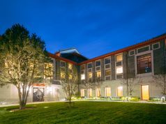 Schwarzman Scholarship 2026 Program in China | Fully Funded A modern three-story building with large windows is lit up at night, surrounded by trees and a well-maintained lawn under a deep blue sky—the perfect setting for Schwarzman Scholarship 2026 scholars to gather and collaborate.