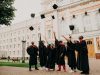 Scholarships for International Students in Canada A group of graduates in black gowns and red stoles, some recipients of Scholarships for International Students, throw their caps in the air while celebrating outside a large university building.