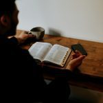 Man reading the Bible at home, surrounded by a cozy atmosphere and warm lighting.