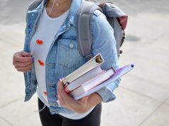 International Student Insurance in Italy: How to Apply in 2025 A student wearing a denim jacket and backpack, covered by international student insurance in Italy, holds several books and notebooks while walking outdoors.