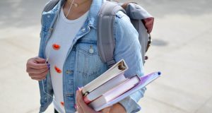 International Student Insurance in Italy: How to Apply in 2025 A student wearing a denim jacket and backpack, covered by international student insurance in Italy, holds several books and notebooks while walking outdoors.