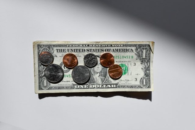 A U.S. one-dollar bill lies flat on a white surface, with coins—including pennies, nickels, dimes, and quarters—arranged on top under bright lighting, symbolizing opportunities like scholarships for international students from Africa.