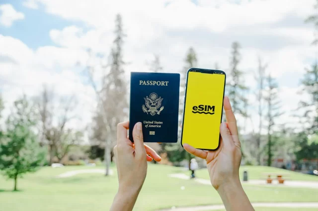 A person holds up a U.S. passport in one hand and a smartphone displaying an eSIM logo in the other, highlighting the importance of avoiding common mistakes when applying for a student visa, with a park and trees blurred in the background.