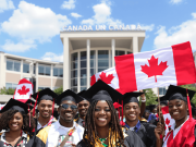 Fully Funded Scholarship in Canada for African students A diverse group of graduates in caps and gowns smile and hold Canadian flags in front of a building with Canada written on it, celebrating their achievement—thanks to a fully funded scholarship in Canada for African students—on a sunny day.