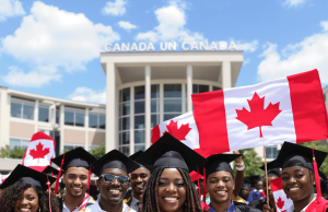 Fully Funded Scholarship in Canada for African students A diverse group of graduates in caps and gowns smile and hold Canadian flags in front of a building with Canada written on it, celebrating their achievement—thanks to a fully funded scholarship in Canada for African students—on a sunny day.