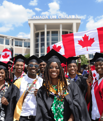 Fully Funded Scholarship in Canada for African students A diverse group of graduates in caps and gowns smile and hold Canadian flags in front of a building with Canada written on it, celebrating their achievement—thanks to a fully funded scholarship in Canada for African students—on a sunny day.