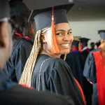 A graduate smiling confidently in cap and gown, celebrating their academic achievement at a graduation ceremony, representing the success of minority students pursuing MBA scholarships.