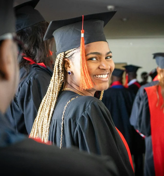 A graduate smiling confidently in cap and gown, celebrating their academic achievement at a graduation ceremony, representing the success of minority students pursuing MBA scholarships.